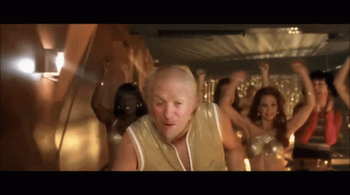 A Group Of People Are Dancing In A Room With A Bald Man In The Foreground GIF