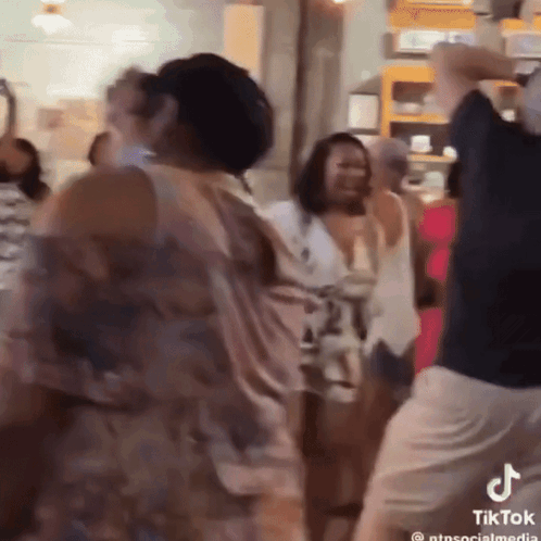 A Group Of People Are Dancing In A Room With A Tiktok Logo On The Bottom Right GIF