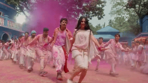 A Group Of People Are Dancing In Front Of A Blue Building Covered In Pink Powder GIF
