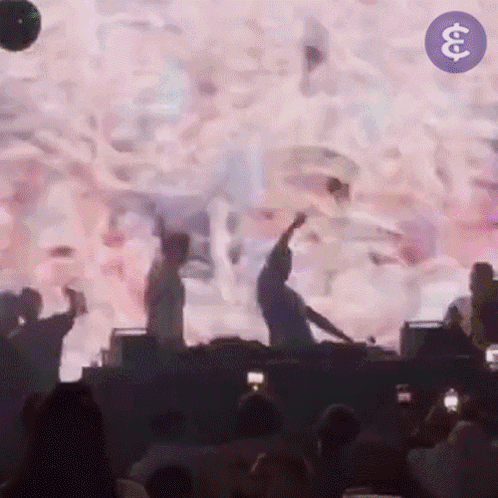 A Group Of People Are Dancing In Front Of A Large Screen With The Letter S On It GIF