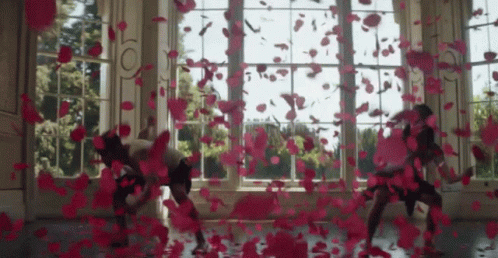 A Group Of People Are Dancing In Front Of A Window With Petals Falling On The Floor GIF