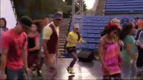 A Group Of People Are Dancing In Front Of Blue Bleachers With Youtube.com In The Bottom Right Corner GIF
