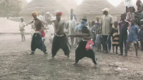 a group of people are dancing in the dirt in front of a crowd