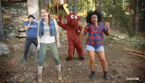 A Group Of People Are Dancing In The Woods With A Mascot In The Middle . GIF