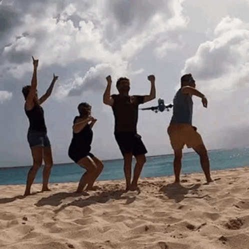 a group of people are dancing on a beach while a plane is flying in the background .