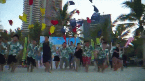 A Group Of People Are Dancing On A Beach With Balloons In The Air GIF
