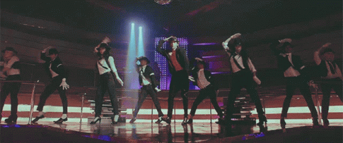 A Group Of People Are Dancing On A Stage In A Dark Room GIF
