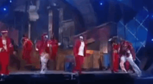 A Group Of People Are Dancing On A Stage In Front Of A Blue Background . GIF