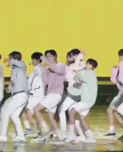 A Group Of People Are Dancing On A Stage In Front Of An Orange Background GIF