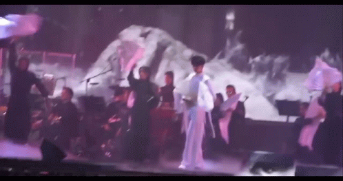 A Group Of People Are Dancing On A Stage While A Man Sings . GIF