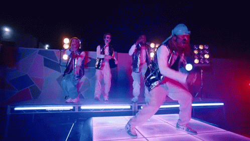 A Group Of People Are Dancing On A Stage With Purple Lights Behind Them GIF