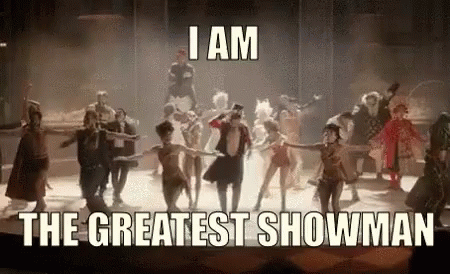 A Group Of People Are Dancing On A Stage With The Words `` I Am The Greatest Showman '' Written Above Them . GIF