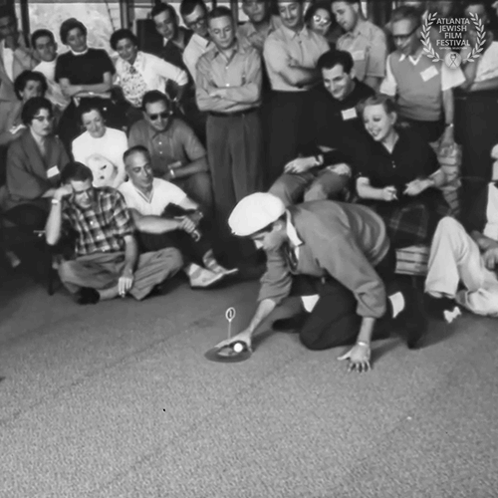A Group Of People Are Gathered Around A Man Kneeling On The Floor Playing A Game With A Ball GIF