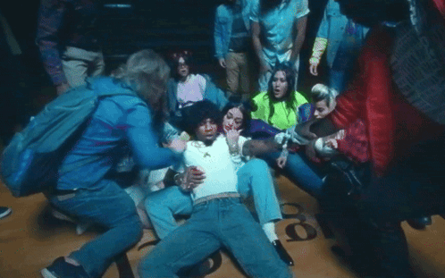 A Group Of People Are Gathered Around A Man Laying On The Floor With The Number 18 On The Ground GIF