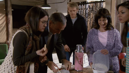a group of people are gathered around a table with a pink thermos with flowers on it