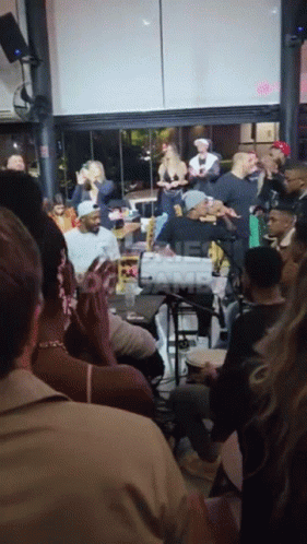 A Group Of People Are Gathered In A Room With A Sign That Says ' One Camp ' In The Corner GIF