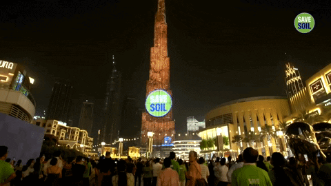 A Group Of People Are Gathered In Front Of A Tower That Says Save Soil On It GIF