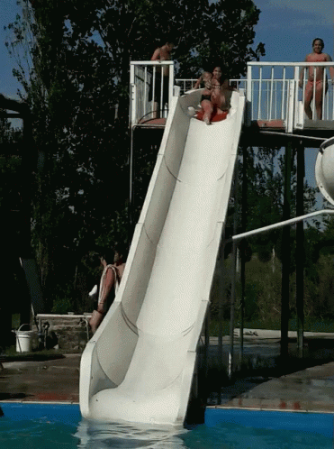 A Group Of People Are Going Down A Slide In A Pool GIF