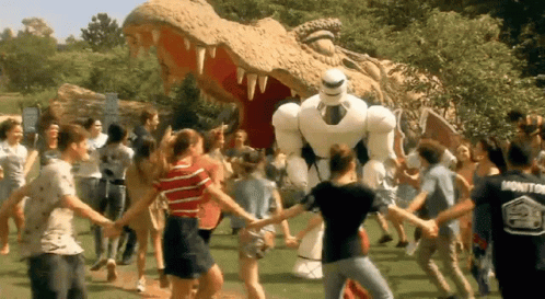 a group of people are holding hands in front of a statue of a dinosaur and a robot