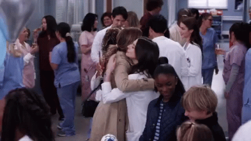 A Group Of People Are Hugging Each Other In A Crowded Room . GIF