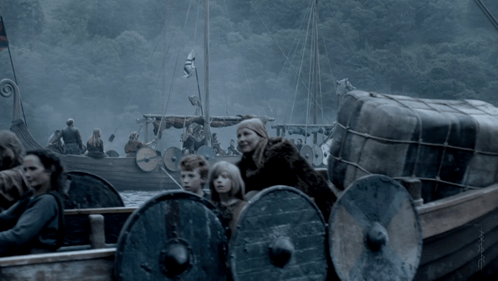 a group of people are in a boat with shields and a large barrel on the back