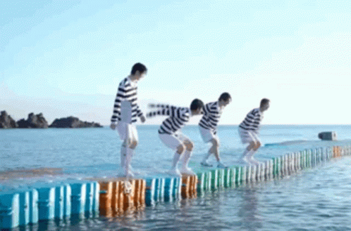 A Group Of People Are Jumping Over A Fence Into The Water . GIF