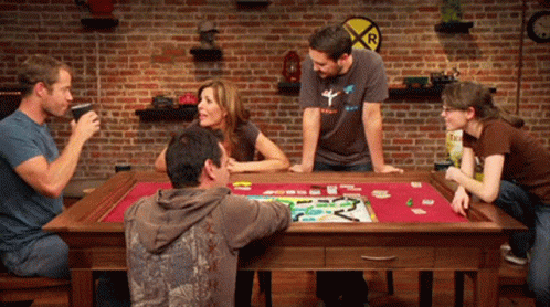 A Group Of People Are Playing A Board Game With A Railroad Crossing Sign In The Background GIF