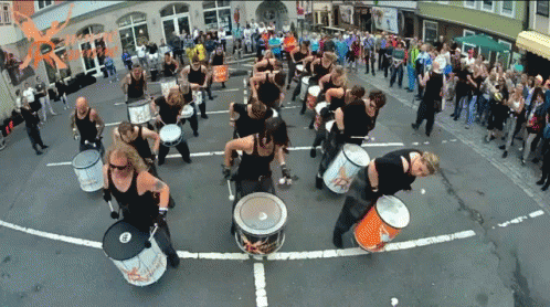A Group Of People Are Playing Drums On A Street With A Sign That Says ' Rhythm ' GIF