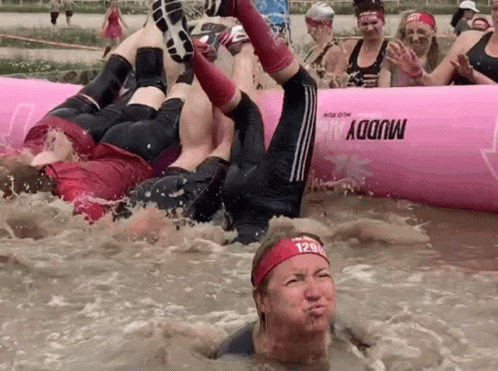 A Group Of People Are Playing In A Muddy Pool With A Pink Raft That Says Muddy On It GIF
