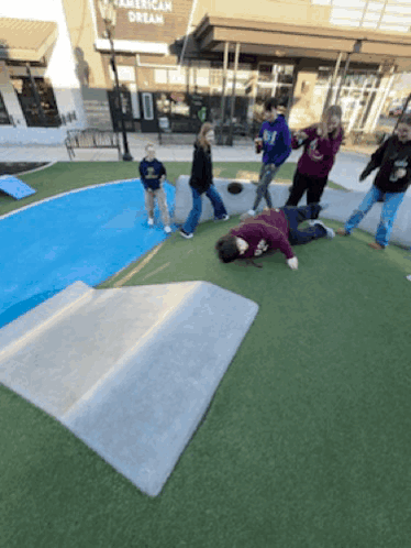 A Group Of People Are Playing In A Park In Front Of An American Dream Store GIF