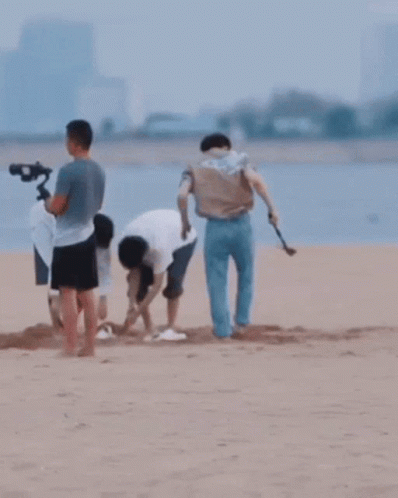 A Group Of People Are Playing In The Sand On A Beach GIF