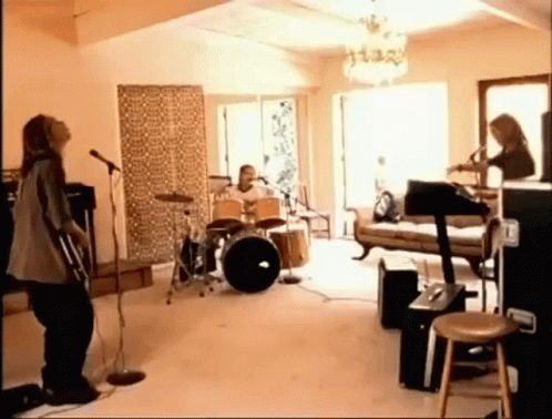 a group of people are playing instruments in a living room while a woman sings into a microphone .