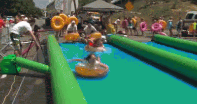 A Group Of People Are Playing On A Water Slide With Tubes . GIF