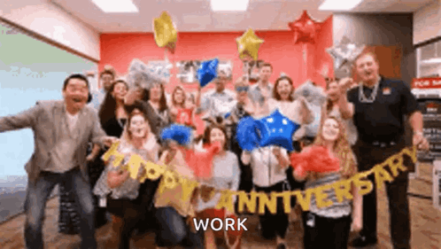 A Group Of People Are Posing For A Picture With Balloons And A Banner That Says Happy Anniversary Work . GIF