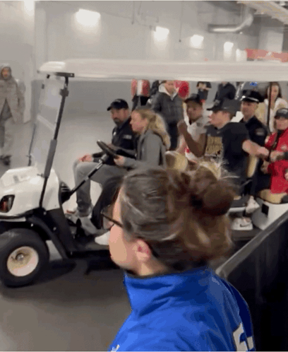 A Group Of People Are Riding In A Golf Cart And One Of Them Is Wearing A Blue Jacket With The Number 4 On It GIF