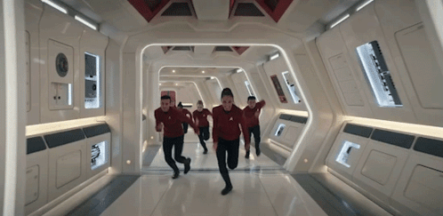 a group of people are running down a hallway in a spaceship .