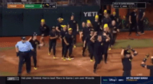 a group of people are running on a baseball field with a scoreboard in the background