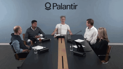 A Group Of People Are Sitting Around A Conference Table With A Palantir Logo Behind Them GIF