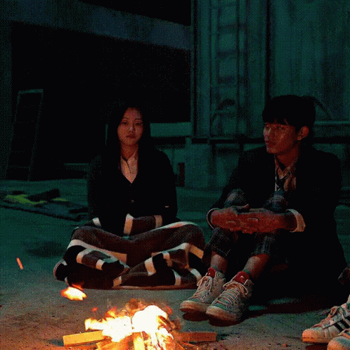 A Group Of People Are Sitting Around A Fire GIF