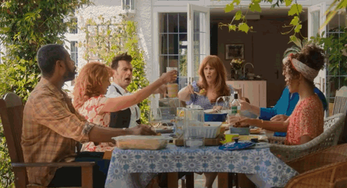 A Group Of People Are Sitting Around A Table Eating Food And Drinking Wine GIF