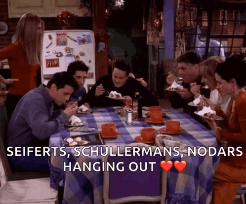 A Group Of People Are Sitting Around A Table Eating Food With The Words Seiferts Schullermans Nodars Hanging Out Above T GIF