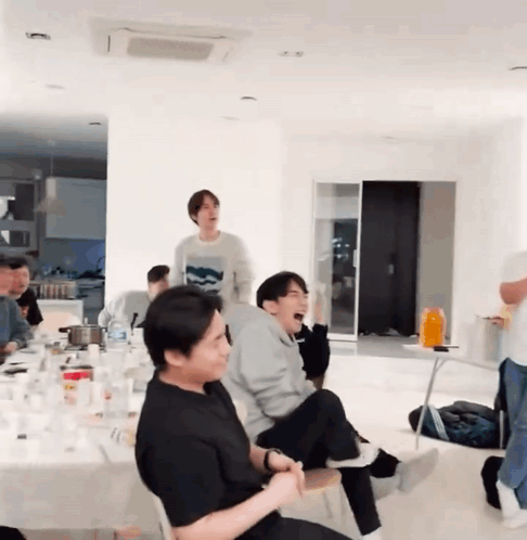 A Group Of People Are Sitting Around A Table In A Living Room . GIF