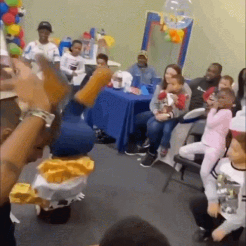 A Group Of People Are Sitting Around A Table In A Room With Balloons . GIF