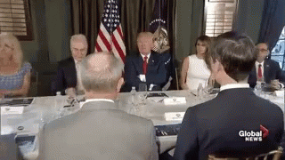 A Group Of People Are Sitting Around A Table With A Man In A Suit . GIF