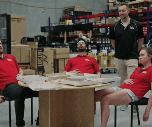 A Group Of People Are Sitting Around A Table With Boxes Of Pizza And A Sign That Says Gt301 GIF