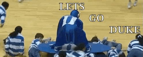 A Group Of People Are Sitting Around A Table With The Words Let 'S Go Duke On The Bottom GIF