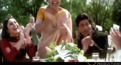 A Group Of People Are Sitting At A Table Clapping And Laughing GIF