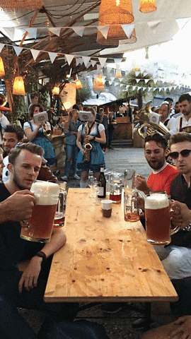 a group of people are sitting at a table holding mugs of beer