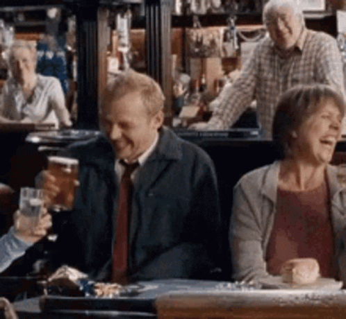 A Group Of People Are Sitting At A Table In A Bar Drinking Beer And Laughing . GIF