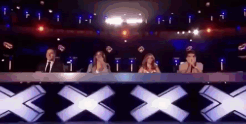 People Sitting At Table In Front Of Stage With X Sign GIF